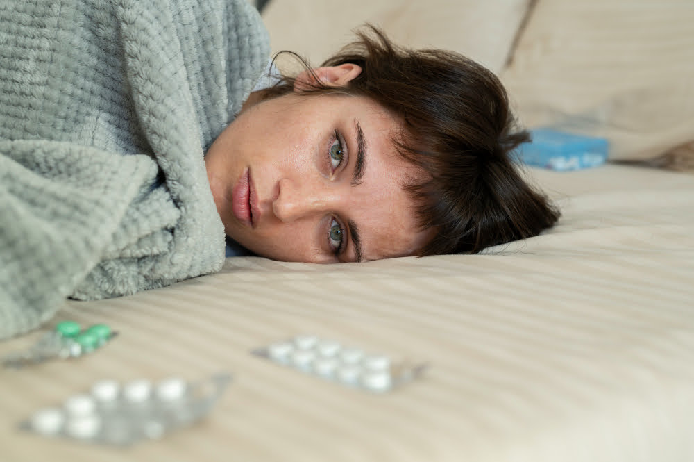 chica tumbada en la cama rodeada de pastillas antipiréticas